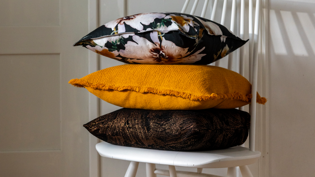 Three interior cushion covers stacked on top of a white wooden chair.