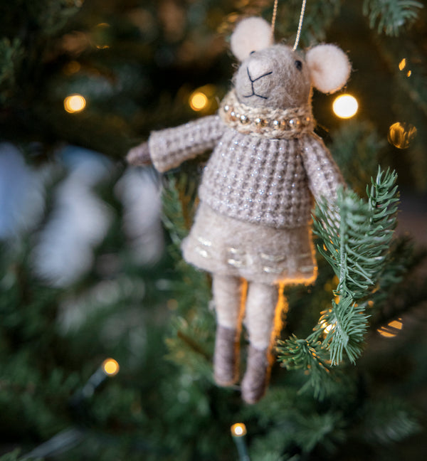 Knitted mouse ornament hanging on a Christmas tree with lights in the background. Redirects to Christmas decoration product collection.