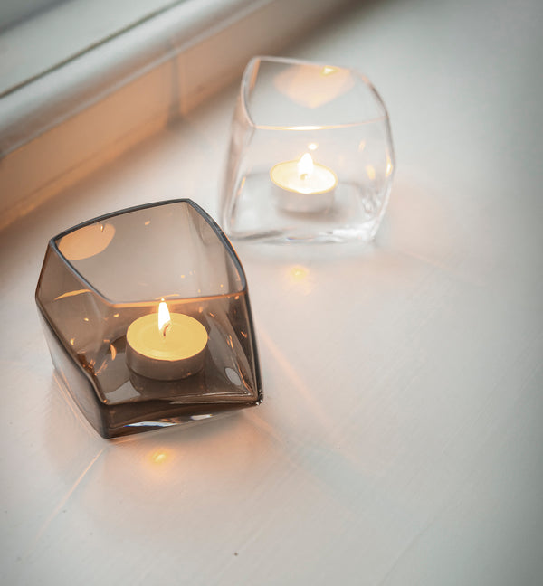 Two Lohkare glass candle holders with lit candles on a light surface. Redirects to Christmas decoration product collection.